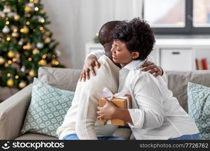 holidays, celebration and people concept - happy african american couple with christmas gift hugging at home. happy african couple with christmas gift at home