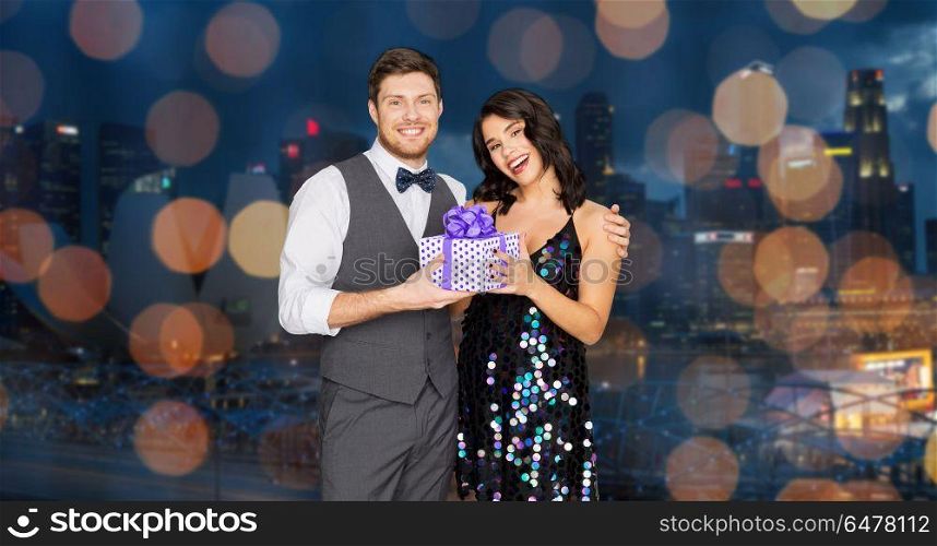 holidays, celebration and people concept - happy couple with gift box at party over singapore city night lights background. happy couple with gift box at birthday party. happy couple with gift box at birthday party
