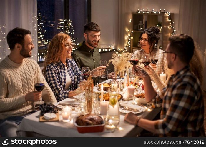 holidays, celebration and people concept - happy friends having christmas dinner at home drinking non-alcoholic red wine. happy friends drinking red wine at christmas party