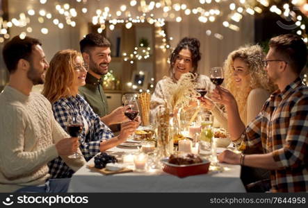 holidays, celebration and people concept - happy friends having christmas dinner at home drinking non-alcoholic red wine. happy friends drinking red wine at christmas party