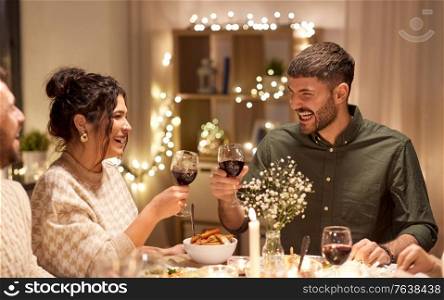 holidays, celebration and people concept - happy friends having christmas dinner party drinking red wine at home. happy friends drinking red wine at christmas party