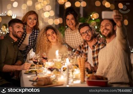 holidays, celebration and people concept - happy friends taking selfie by smartphone at home christmas dinner party. friends taking selfie at christmas dinner party