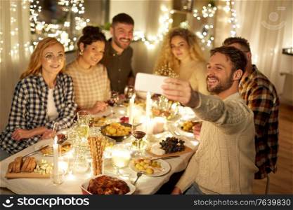 holidays, celebration and people concept - happy friends taking selfie with smartphone at home christmas dinner party. friends taking selfie at christmas dinner party
