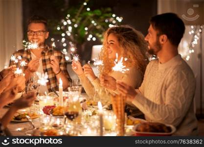 holidays, celebration and people concept - happy friends with sparklers having christmas dinner at home. happy friends having christmas dinner at home