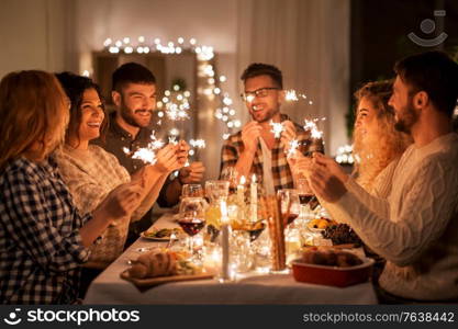 holidays, celebration and people concept - happy friends with sparklers having christmas dinner at home. happy friends having christmas dinner at home