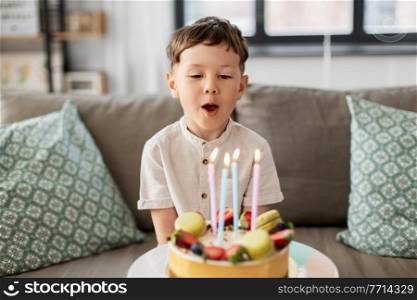 holidays, celebration and people concept - happy little boy blowing candles on birthday cake at home party. happy little boy blowing candles on birthday cake