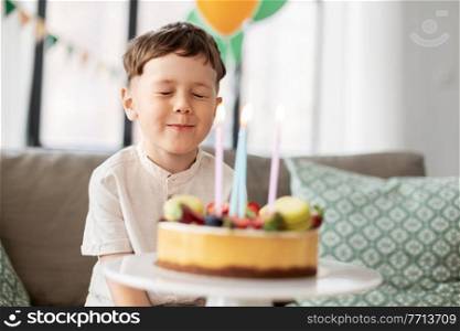 holidays, celebration and people concept - happy little boy with birthday cake making wish at home party. little boy with birthday cake making wish