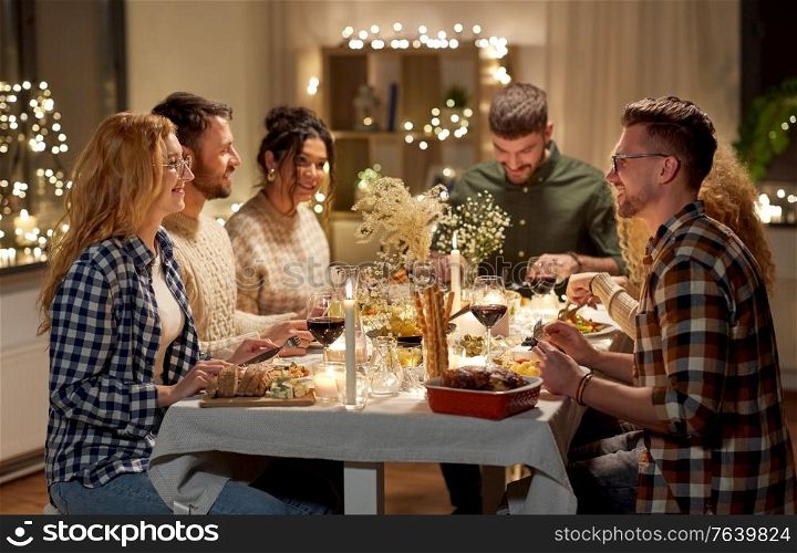 holidays, celebration and people concept - happy smiling friends having christmas dinner party at home in evening. happy friends having christmas dinner at home
