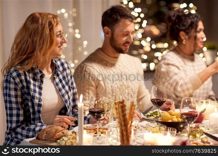 holidays, celebration and people concept - happy smiling friends having christmas dinner party at home in evening. happy friends having christmas dinner at home