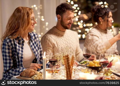 holidays, celebration and people concept - happy smiling friends having christmas dinner party at home in evening. happy friends having christmas dinner at home