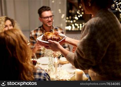 holidays, celebration and people concept - happy smiling friends having roast chicken or duck for christmas dinner at home in evening. happy friends having christmas dinner at home