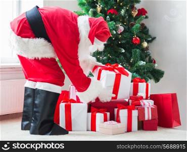 holidays, celebration and people concept - man in costume of santa claus putting present under christmas tree