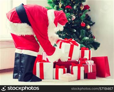 holidays, celebration and people concept - man in costume of santa claus putting present under christmas tree