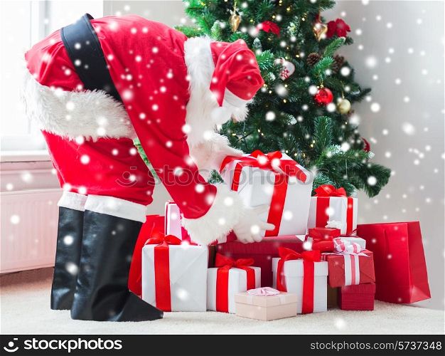 holidays, celebration and people concept - man in costume of santa claus putting present under christmas tree at home