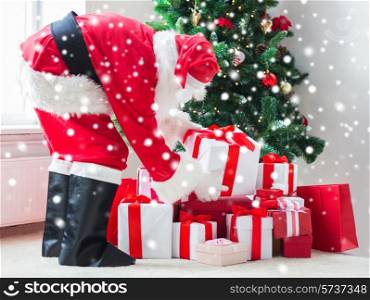 holidays, celebration and people concept - man in costume of santa claus putting present under christmas tree at home