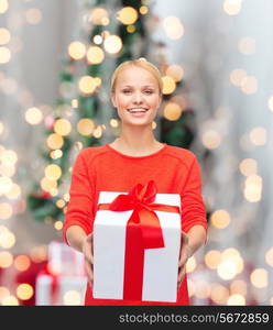 holidays, celebration and people concept - smiling woman in red clothes with gift box over christmas tree and ligths background