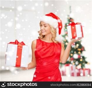 holidays, celebration and people concept - smiling woman in santa helper hat and red dress with gift boxes over living room and christmas tree background