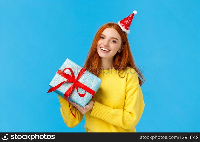 Holidays, celebration and presents concept. Cheerful redhead girl love christmas, enjoy celebrating with friends, receive gift in wrapped box from secret santa, wearing cute hat, blue background.. Holidays, celebration and presents concept. Cheerful redhead girl love christmas, enjoy celebrating with friends, receive gift in wrapped box from secret santa, wearing cute hat, blue background