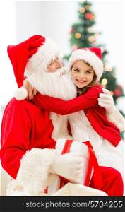 holidays, celebration, childhood and people concept - smiling little girl hugging with santa claus over christmas tree lights background