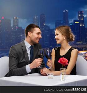 holidays, celebration, dating and people concept - smiling couple clinking glasses of champagne and looking to each other at restaurant over night city background
