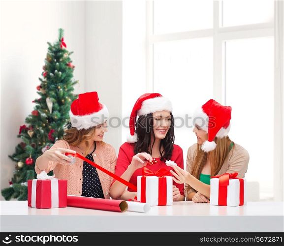 holidays, celebration, decoration and people concept - smiling women in santa helper hats with decorating paper and gift boxes over living room and christmas tree background