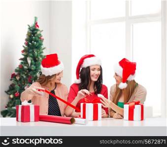 holidays, celebration, decoration and people concept - smiling women in santa helper hats with decorating paper and gift boxes over living room and christmas tree background