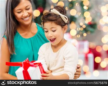 holidays, celebration, family and people concept - happy mother and little girl with gift box over living room and christmas tree background