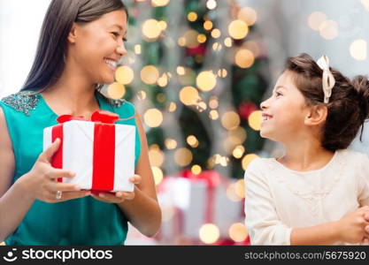 holidays, celebration, family and people concept - happy mother and little girl with gift box over living room and christmas tree background