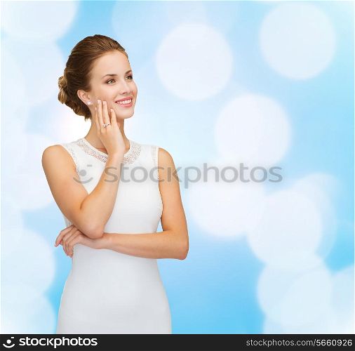 holidays, celebration, wedding and people concept - smiling woman in white dress wearing diamond ring over blue lights background