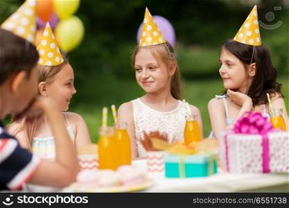 holidays, childhood and celebration concept - happy kids sitting at table on birthday party at summer garden. happy kids on birthday party at summer garden. happy kids on birthday party at summer garden