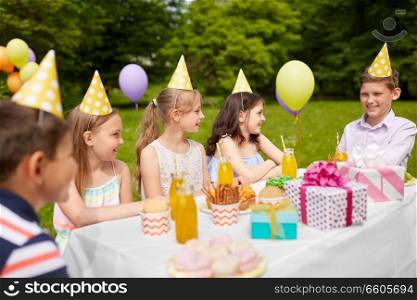 holidays, childhood and celebration concept - happy kids sitting at table on birthday party at summer garden. happy kids on birthday party at summer garden