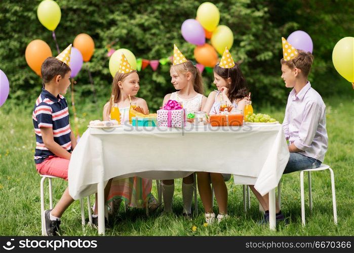 holidays, childhood and celebration concept - happy kids sitting at table on birthday party at summer garden. happy kids on birthday party at summer garden. happy kids on birthday party at summer garden
