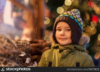 holidays, childhood and people concept - happy little boy at christmas market in winter evening. happy little boy at christmas market in winter