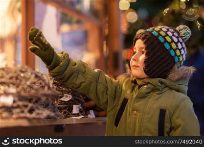 holidays, childhood and people concept - happy little boy at christmas market in winter evening. happy little boy at christmas market in winter