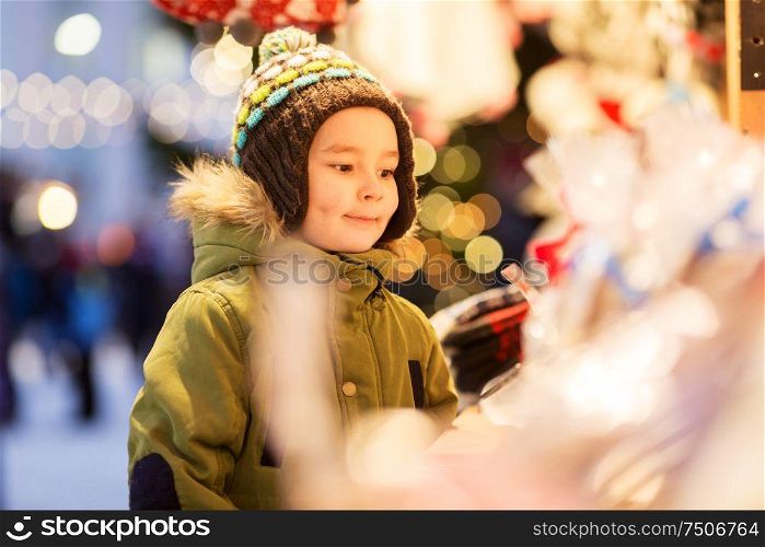 holidays, childhood and people concept - happy little boy at christmas market stall in winter evening. happy little boy at christmas market in winter