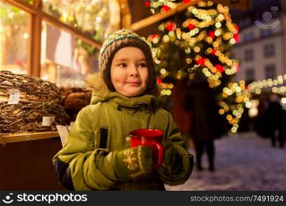 holidays, childhood and people concept - happy little boy with cup of tea at christmas market in winter evening. happy boy with cup of tea at christmas market