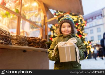 holidays, childhood and people concept - happy little boy with gift box at christmas market in winter evening. happy boy with gift box at christmas market