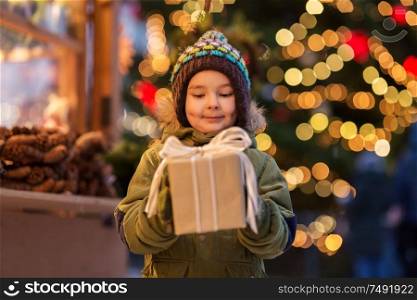 holidays, childhood and people concept - happy little boy with gift box at christmas market in winter evening. happy boy with gift box at christmas market