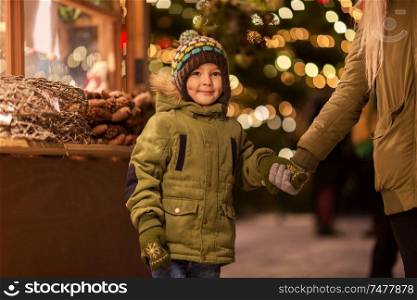 holidays, childhood and people concept - happy little boy with mother at christmas market in winter evening. happy little boy with mother at christmas market