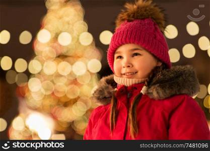 holidays, childhood and people concept - happy little girl at christmas market in winter evening. happy little girl at christmas market in winter