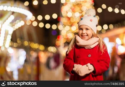 holidays, childhood and people concept - happy little girl at christmas market in winter evening. happy little girl at christmas market in winter