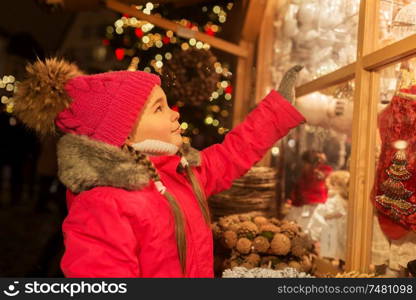 holidays, childhood and people concept - happy little girl choosing christmas decorations at market in winter. girl choosing christmas decorations at market