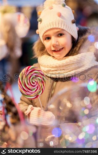 holidays, childhood and people concept - happy little girl with big lollipop at christmas market. litle girl with big lollipop at christmas market