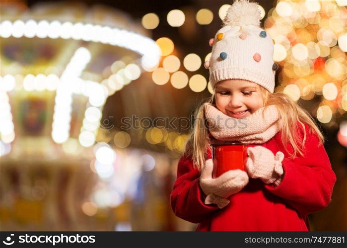 holidays, childhood and people concept - happy little girl with cup of tea at christmas market in winter evening. happy girl with cup of tea at christmas market