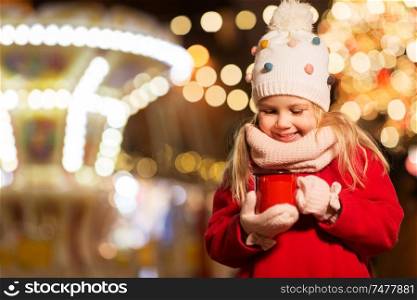 holidays, childhood and people concept - happy little girl with cup of tea at christmas market in winter evening. happy girl with cup of tea at christmas market