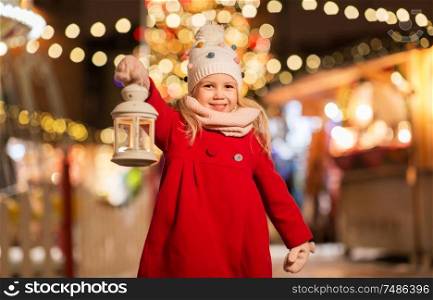 holidays, childhood and people concept - happy little girl with lantern at christmas market in winter evening. happy little girl at christmas with lantern market