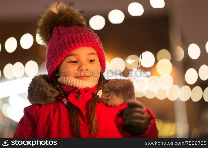 holidays, childhood and people concept - happy little girl with sparkler at christmas market in winter evening. happy girl with sparkler at christmas market