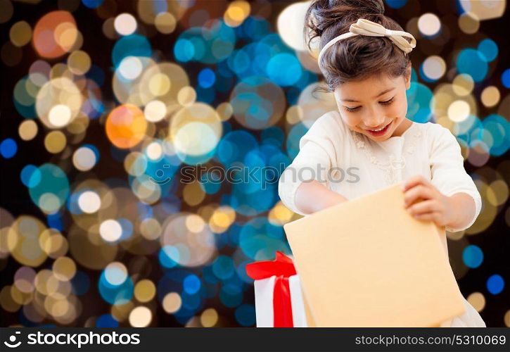 holidays, childhood and people concept - smiling little girl opening gift box over lights background. smiling little girl with gift box over lights