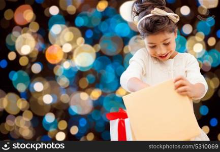holidays, childhood and people concept - smiling little girl opening gift box over lights background. smiling little girl with gift box over lights