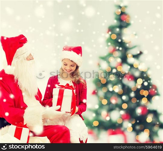 holidays, childhood and people concept - smiling little girl, santa claus with gifts over living room, christmas tree and snow background